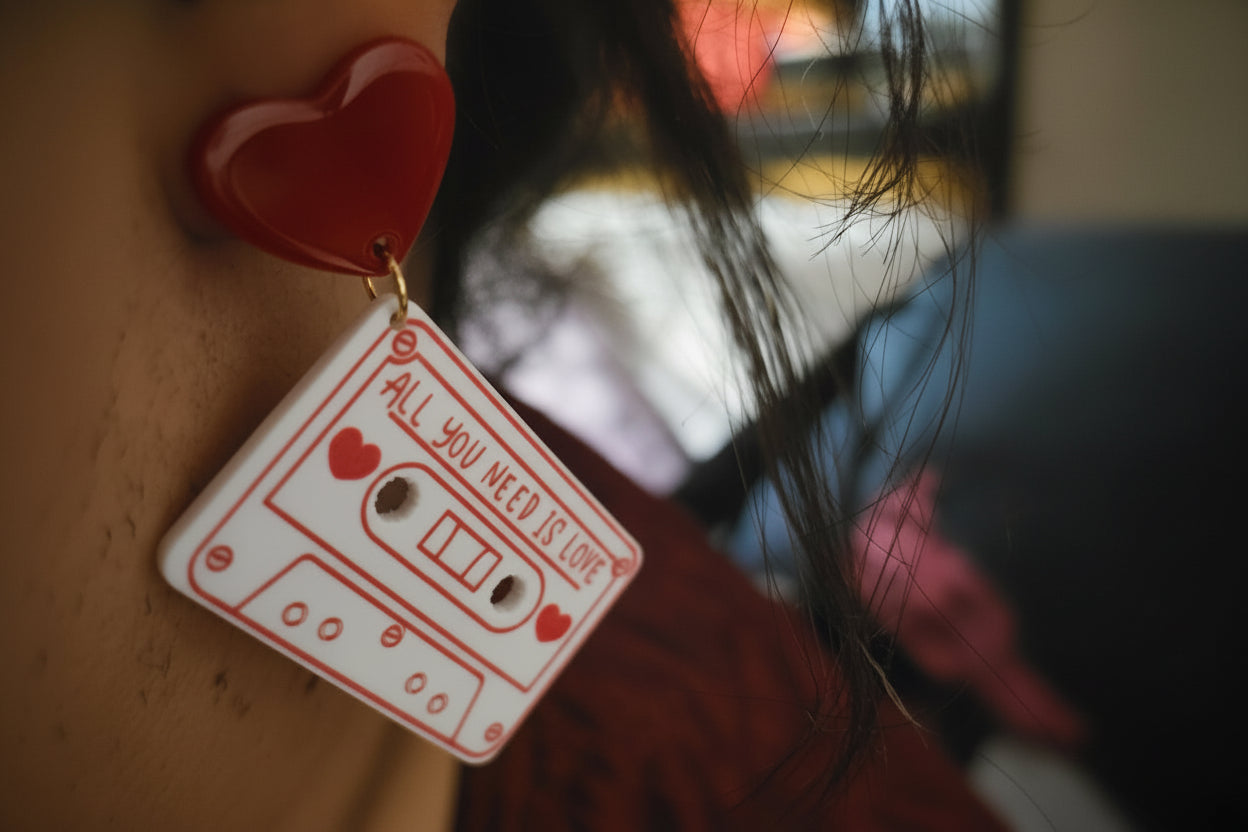 Earring shaped like a cassette tape with 'All You Need Is Love' text and heart symbols.
