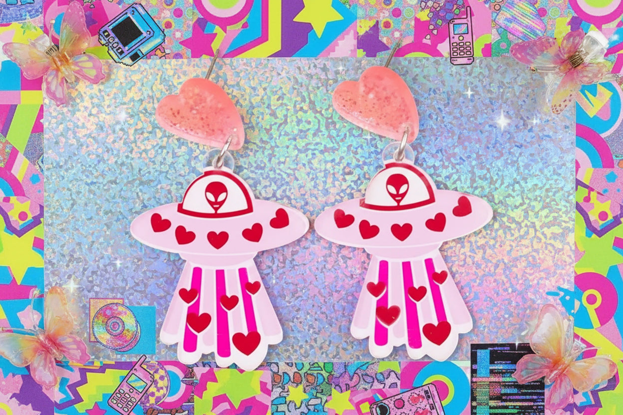Pair of earrings shaped like UFOs with red hearts on a beige background